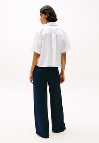 White linen short-sleeve shirt with a back seam detail, paired with navy wide-leg trousers in a smooth fabric.