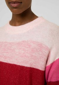 Randig stickad tröja med mjuk struktur; har rosa, ljusrosa och röda band. Rund halsringning och lätt lös passform.