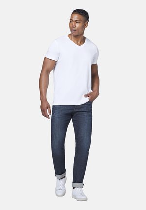 White V-neck t-shirt paired with dark blue denim jeans and white sneakers. The outfit features a casual, fitted design with rolled cuffs.