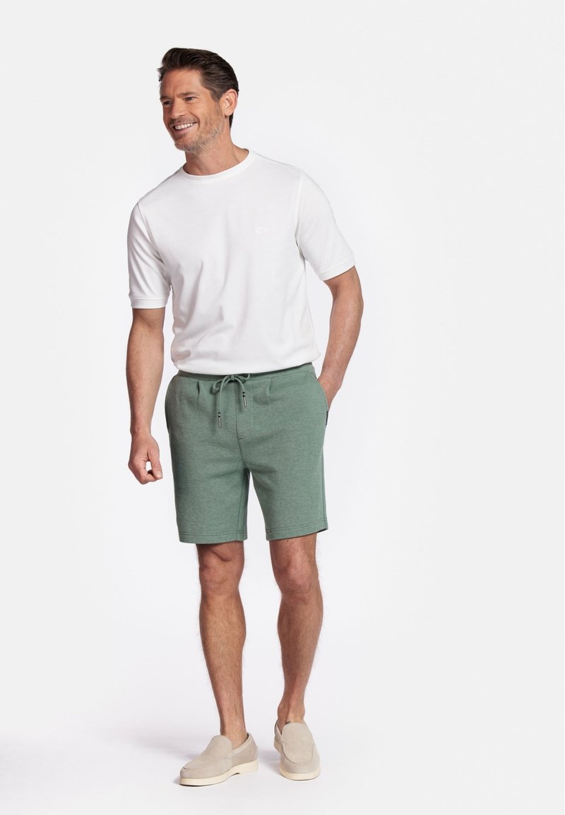 Men's outfit featuring a white crew-neck t-shirt and green drawstring shorts. Shorts have textured fabric and pockets. Tan slip-on shoes.