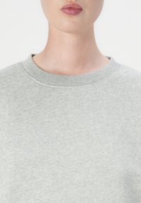 Sweatshirt gris à col ras du cou avec un tissu texturé, présentant un col en bords-côtes et une coupe légèrement ample. Design épuré et minimaliste.