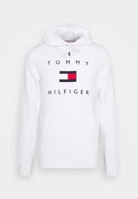 Sudadera blanca de algodón con un bolsillo frontal tipo pouch. Presenta el texto impreso "TOMMY HILFIGER" y un pequeño logo en rojo, azul y blanco.