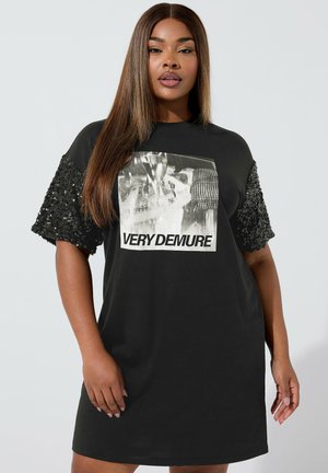 Abito t-shirt nero oversize con maniche corte in paillettes e una grafica frontale che recita "VERY DEMURE". Tessuto morbido e vestibilità comoda.
