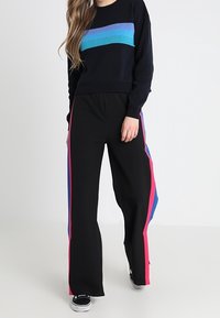 Suéter de la marina con rayas azules horizontales, combinado con pantalones negros que presentan rayas laterales en rosa y azul. Zapatillas negras completan el atuendo.