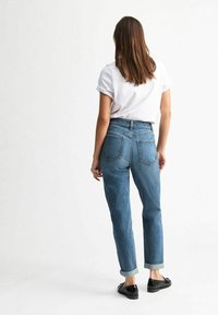 Blauwe high-waisted jeans met een gestructureerde afwerking, opgerolde manchetten en een slanke rechte pijp. Gecombineerd met een wit shirt met korte mouwen.