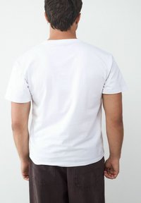 Weißes Baumwoll-T-Shirt mit rundem Ausschnitt, kurzen Ärmeln und geradem Schnitt. Die Rückansicht zeigt ein schlichtes Design ohne Muster oder Verzierungen.