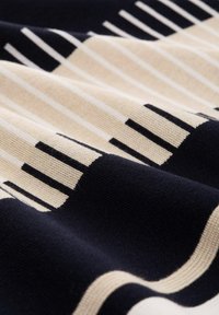 Tissu tricoté présentant des rayures alternées noires et crème avec des détails texturés, créant un motif en vagues à travers le matériau.