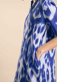 Niebieska i jasnoniebieska oversize sukienka w zwierzęcy wzór, z kołnierzykiem i bocznymi kieszeniami, wykonana z lekkiego materiału.