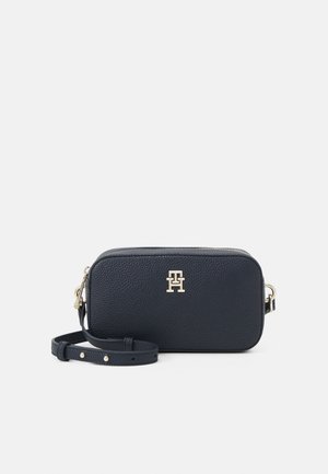 Sac bandoulière en cuir marine avec logo doré, fermeture zip, bandoulière réglable et surface texturée. Forme rectangulaire avec bords arrondis.