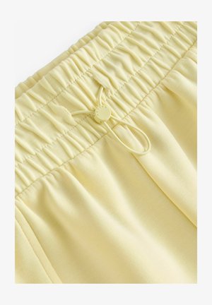 Kollased elastse vöökoha lühikesed püksid kogutud tekstuuriga, reguleeritava nööriga ja sileda kangaga. Lihtne disain ilma mustrite või aktsentideta.