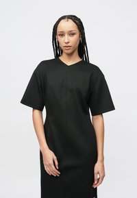 Μαύρο φόρεμα μήκους μέχρι το γόνατο από λεία ύφανση, με ντεκολτέ V και κοντά μανίκια. Διαθέτει ελάχιστες ραφές και ίσια γραμμή.