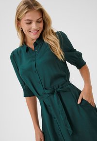 Abito camicia in tessuto verde scuro, con abbottonatura frontale, maniche corte a palloncino con arricciature, cintura da annodare e tasche laterali.