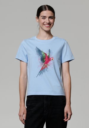 T-shirt en coton bleu clair avec un graphique de perroquet coloré agrémenté d'accents verts et rouges, encolure ronde et manches courtes.