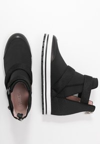 Zwarte enkelboots van textuurmateriaal met elastische banden, een gewatteerde kraag en een witte rubberen zool. Strakke, moderne uitstraling.