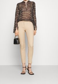 Sheer black striped blouse with a tie neckline, paired with beige fitted pants and black strappy heeled sandals. Small black handbag.