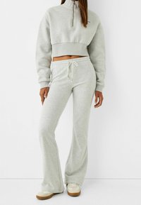 Felpa grigia cropped con collo a mezza zip e pantaloni abbinati con vestibilità ampia. Materiale morbido con vita regolabile, vestibilità comoda.