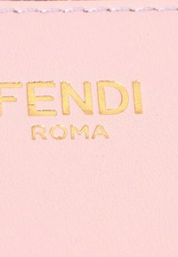 Texte embossé doré « FENDI ROMA » sur fond en cuir texturé rose clair avec surpiqûres visibles en haut.