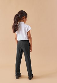 Vit kortärmad blus i kombination med svarta figurnära byxor, sedd bakifrån. Outfiten kompletteras av mörka skor. Enkel design.