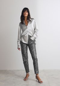 Chemise boutonnée en satin argenté, coupe ample ; pantalon léopard noir et gris ; talons aiguilles strappy argentés brillants ; textures lisses tout au long.