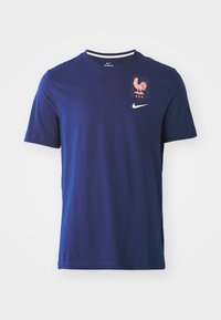 Vyriška mėlyna medvilninė marškinėliai su apvalia iškirpte, su rožiniu gaidžio emblema ir balta Nike logotipu ant krūtinės. Trumpomis rankovėmis, standartinis kirpimas.