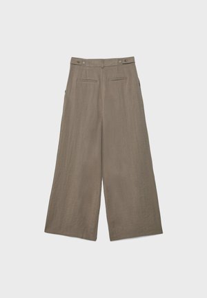 Beige hørbukser med vide ben, justerbare sider og baglommer med kant, vist fladt på en lys baggrund.