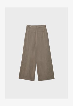 Béžové ľanové nohavice so širokými nohavicami, bočnými nastavovacími pásikmi a zadnými klopovými vreckami, zobrazené položené na svetlom pozadí.