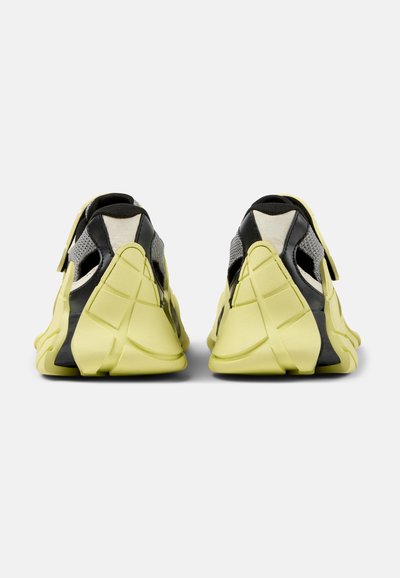 Footwear features a sleek design with a predominantly yellow rubber upper, black and gray accents, and textured detailing on the sides.
