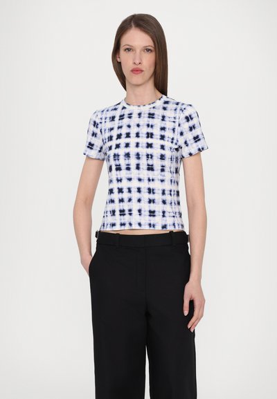 Short-sleeve crop top in white and navy tie-dye pattern. Smooth fabric with a fitted design and crew neckline. Paired with black trousers.