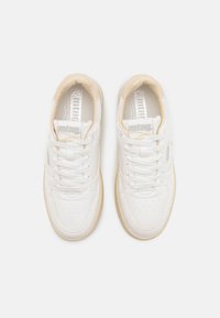 Baskets blanches avec une tige en cuir lisse, des accents texturés, des lacets blancs et une semelle en caoutchouc crème. Présente un logo sur la languette.