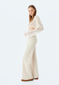 Gehaakte crop top met lange mouwen in crème, gecombineerd met wijdvallende beige broek met structuur en bruine enkellaarsjes.