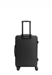 Valise rigide noire avec une poignée télescopique extensible et quatre roues pivotantes sur fond blanc.