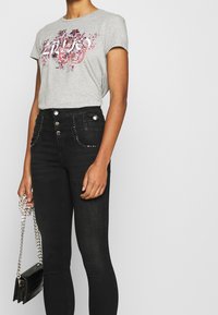 Camiseta gris de manga corta con estampado floral, combinada con jeans negros de talle alto con cierre de botones y bolsillos con tachuelas.