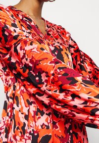 Flowing dress with a V-neck, featuring a vibrant red, pink, and black abstract pattern. Long sleeves, soft fabric, and a relaxed fit.