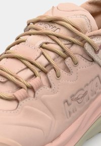 Baskets de sport rose pâle avec cuir texturé, lacets ronds contrastants et logo en relief sur le côté. Semelle douce et rembourrée.