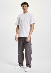 White cotton t-shirt with short sleeves, paired with gray cargo pants featuring multiple pockets, worn with white sneakers.