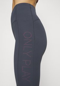 Leggings blu navy con vita alta, caratterizzati da testo a pois rosa "ONLY PLAY" lungo il lato, texture liscia e dettagli di cucitura a contrasto.