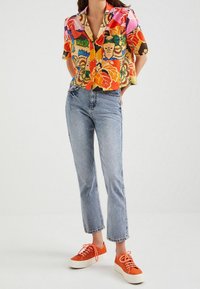 Kortærmet, farverig blomsterprint skjorte med kontrasterende mønstre, parret med lys blå lige ben jeans og orange sneakers med hvide såler.