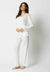 Hvid pyjamas sæt med en knapfront top med blonde detaljer på skuldrene og lange ærmer, parret med matchende lige benbukser.