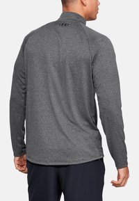 Grå langærmet sportsbluse med høj krave, med struktureret stof og et logo på den øverste del af ryggen. Langærmede og tætsiddende design.