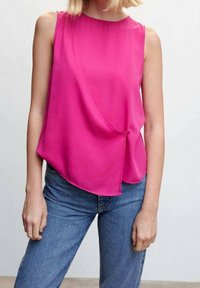 Haut sans manches fuchsia, en tissu lisse, doté d'un ourlet asymétrique et d'un détail nœud sur le côté. Associé à un jean denim bleu.