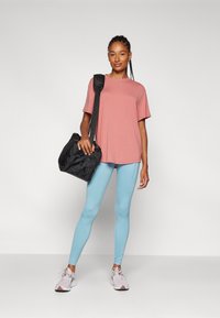 Camisetta rosa a maniche corte, leggings azzurri chiari e scarpe da ginnastica rosa. Una borsa nera con tracolla è portata nella mano sinistra.