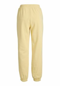 Lys gule strikkede joggebukser med elastisk midje og mansjetter. Myk tekstur, løs passform, ingen synlige mønstre eller detaljer med hardware.
