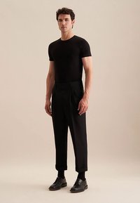 T-shirt noir ajusté associé à un pantalon noir taille haute avec plis. Complété par des chaussures noires à lacets et des chaussettes montantes.