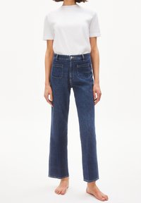 Modré jeans s rovnými nohavicemi, vysokým pasem a dvěma zadními kapsami. Kombinované s jednoduchým bílým tričkem s krátkým rukávem.