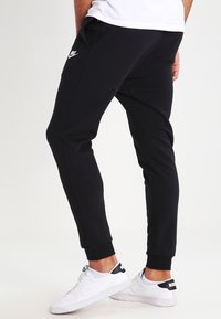 Pantaloni della tuta neri realizzati in tessuto misto cotone, con design affusolato, vita elastica e logo Nike sulla coscia sinistra.