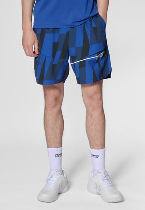 Blå mönstrade shorts med geometriska former. Har fickor och en vit dragkedjeflik. Matchas med vita sportskor och strumpor.