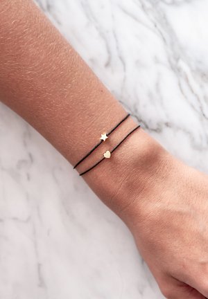 Braccialetti in corda nera con charm a forma di stella e cuore in oro. Texture liscia, design minimalista e accenti sottili migliorano l'appeal visivo.