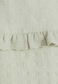 Textured light green fabric with a grid pattern and ruffled hem. Features a soft, woven texture, creating a layered appearance.