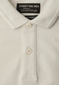 Polo beige clair en tissu texturé, avec deux boutons et une étiquette noire indiquant "Street One Men, Experience Unmatched Comfort."