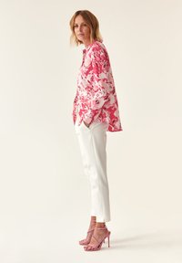 Bluse med blomsterprint i pink, parret med hvide skræddersyede bukser og lyserøde strophæle. Glat, letvægtsstof med afslappet pasform.